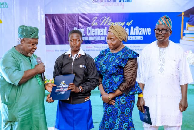 A milestone award: A female scholar is presented with her merit-based folder on stage, surrounded by dignitaries.