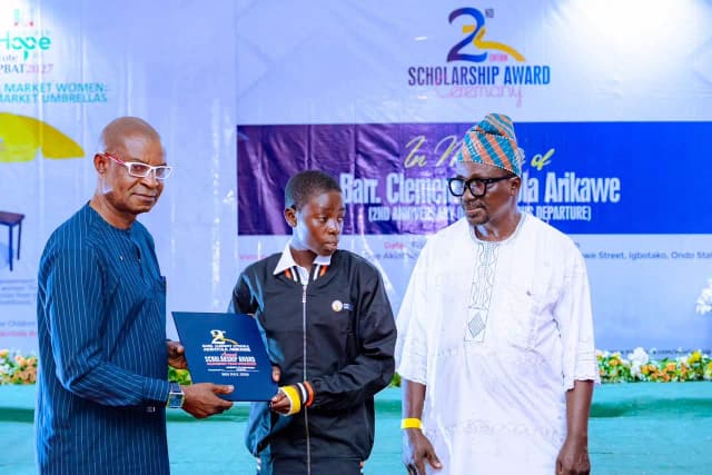 Path to success: A female student receives her merit scholarship folder on stage from community dignitaries.