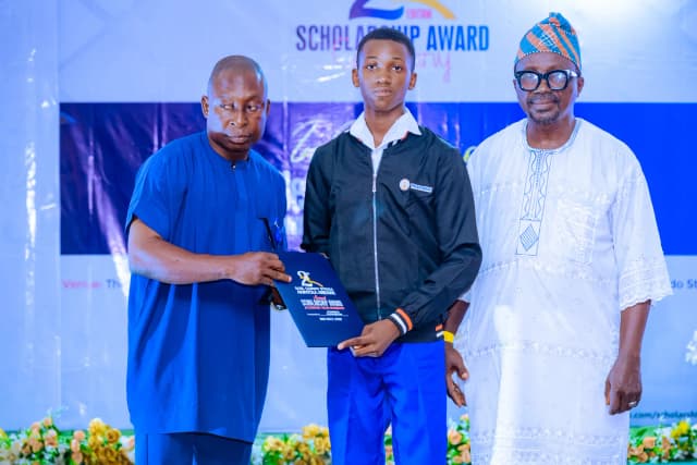 A pathway to growth: A male scholar stands with organizers as his scholarship folder is presented on stage.