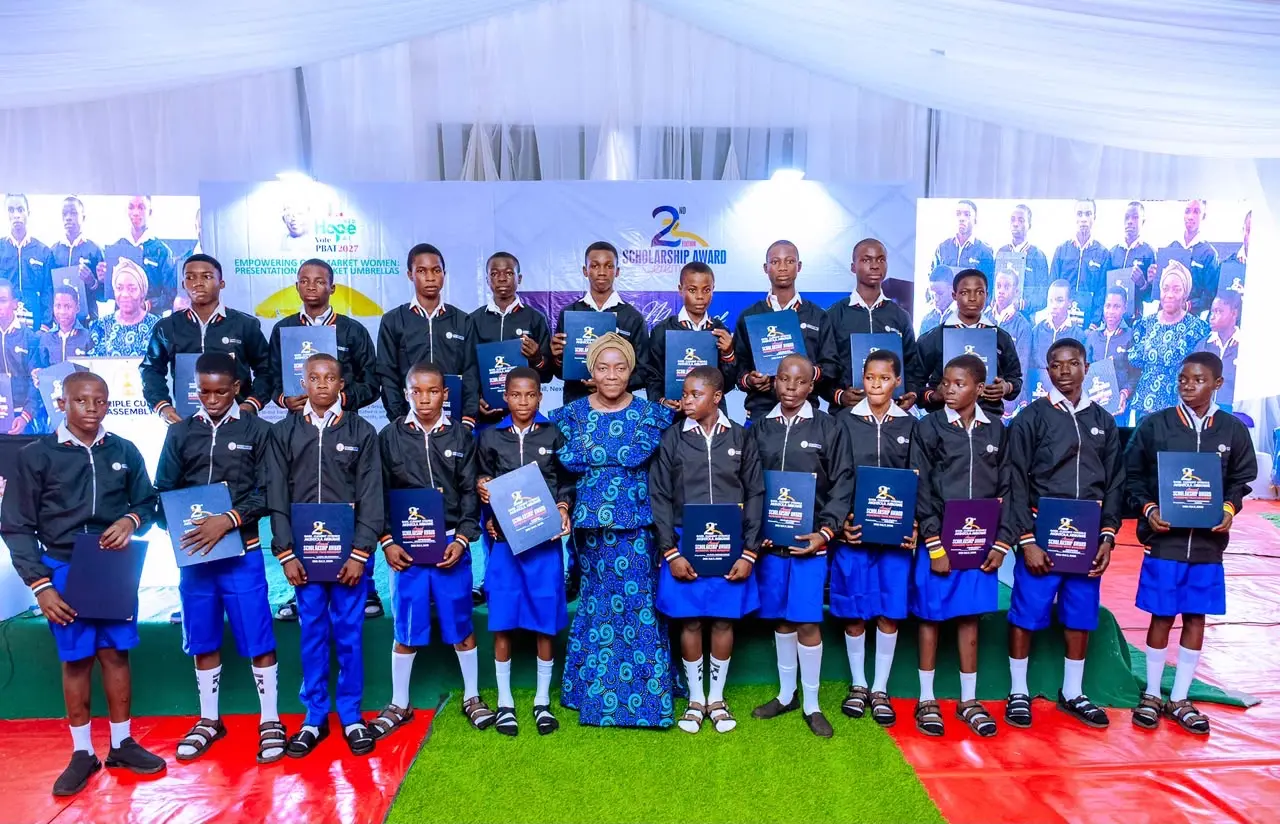 A proud commemorative group portrait of the 2026 scholarship recipients holding their award folders of academic excellence on stage, standing with Arikawe family trustees.